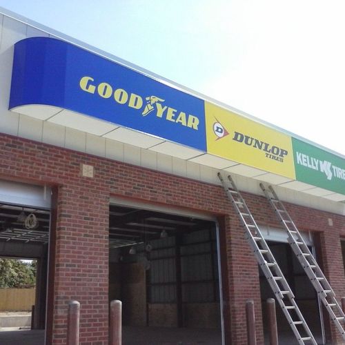 A canvas awning above a mechanic's shop reads advertises several brands - Good Year - Dunlop Tires - Kelly Ties