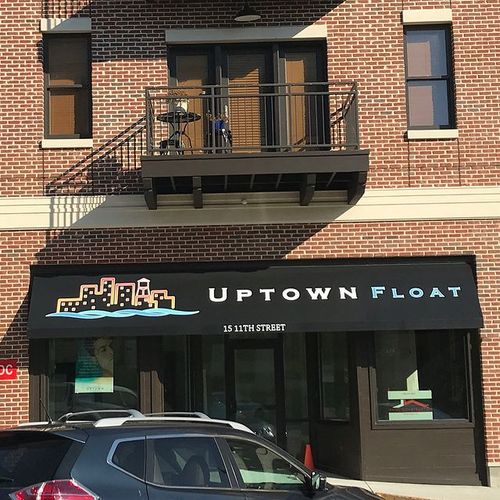 A storefront awning covers the entrance to a street-facing business. The awning reads 'Uptown Float' with an outline of a city beside the water. The address '15 11th Street' is also present on the awning.