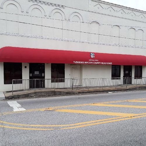 A long bullnose awning that reads 'Tuskegee-Macon County Head Start' covers the walkway in front of a large building