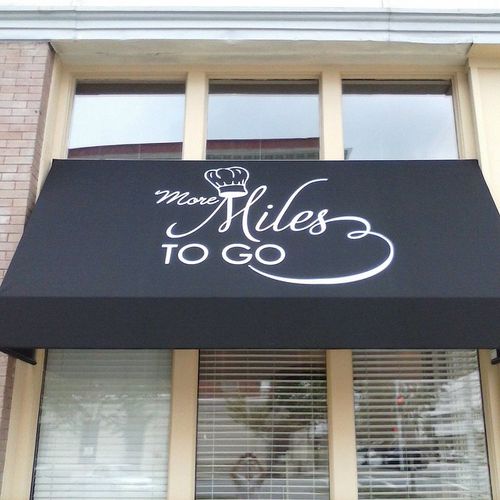 A window awning reads 'More Miles to Go' and partially covers a window to a brick business.