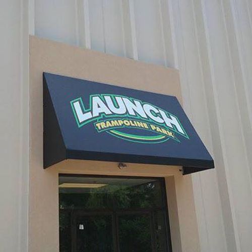 A door awning attached to a large metal-sided building advertises the entrance to Launch Trampoline Park