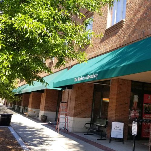 Two long storefront awnings read 'The Market on Broadway' shade the entrances to a large brick building