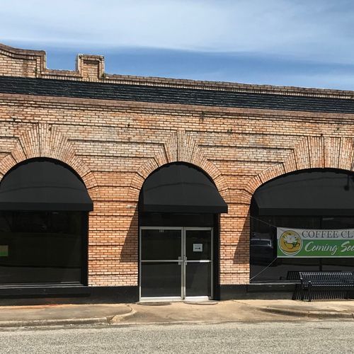 A series of door and window awnings span the side of a long brick building, a sign in a window reads 'Coffe Club - Coming Soon!'