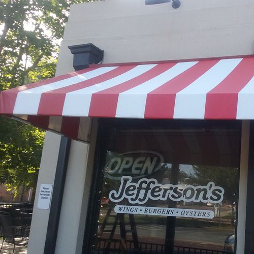 A restaurant window, shaded by a striped awning, reads 'Open - Jefferson's - Wings - Burgers - Oysters'