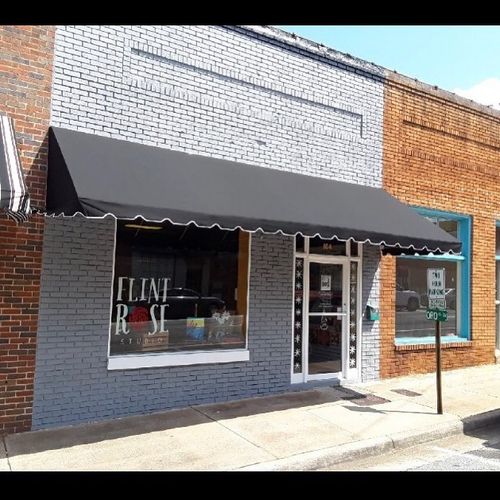 A storefront awning shades the walkway in front of a brick store whose window reads 'Flint Rose Studio'