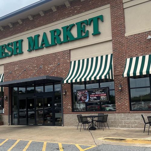 Several canvas window awnings and a metal door awning shade the outside of a Fresh Market building