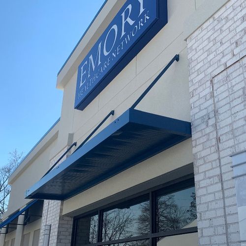 A metal awning covers the entrance of Emory Healthcare Network. Several decorate canvas awnings are present as well.