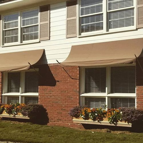 Two first-story windows with flower planters are covered by spearhead window awnings