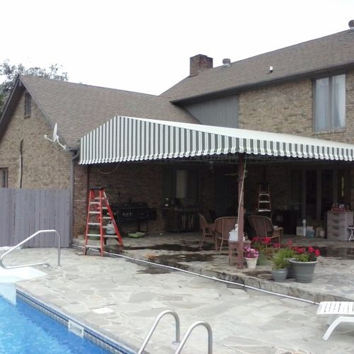 A large, striped patio cover attached to a 2-story home. A small portion of a pool can be seen next to the patio cover.