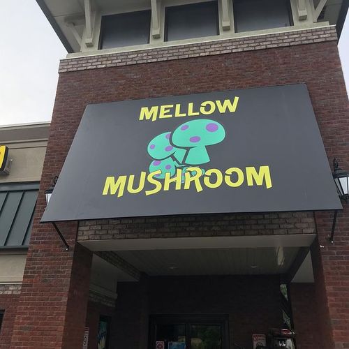 An awning that reads 'Mellow Mushroom' with an image of several mushrooms covers the entrance to a brick building