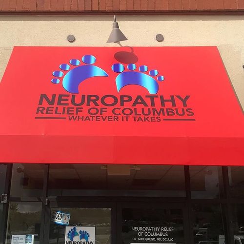 A door awning with an image of two footprints covers the entrance to a building and reads 'Neuropathy Relief of Columbus - Whatever It Takes'
