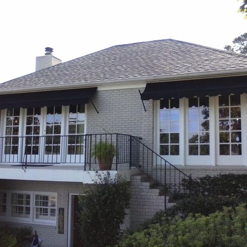 Two long window awnings cover several sets of windows on the second story of a two-story brick home